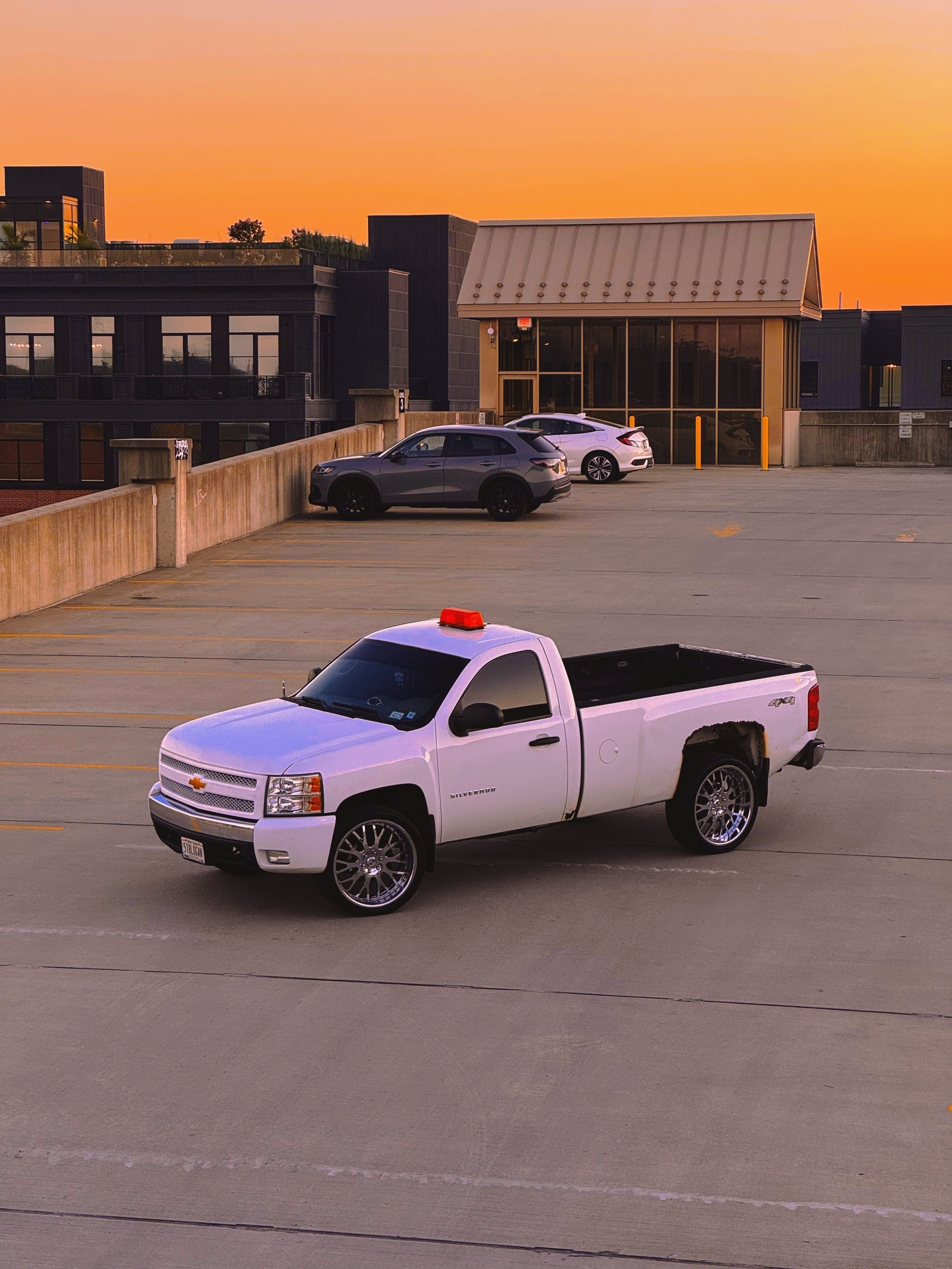 White pickup truck on a rooftop parking lot with buildings in the background during sunset.